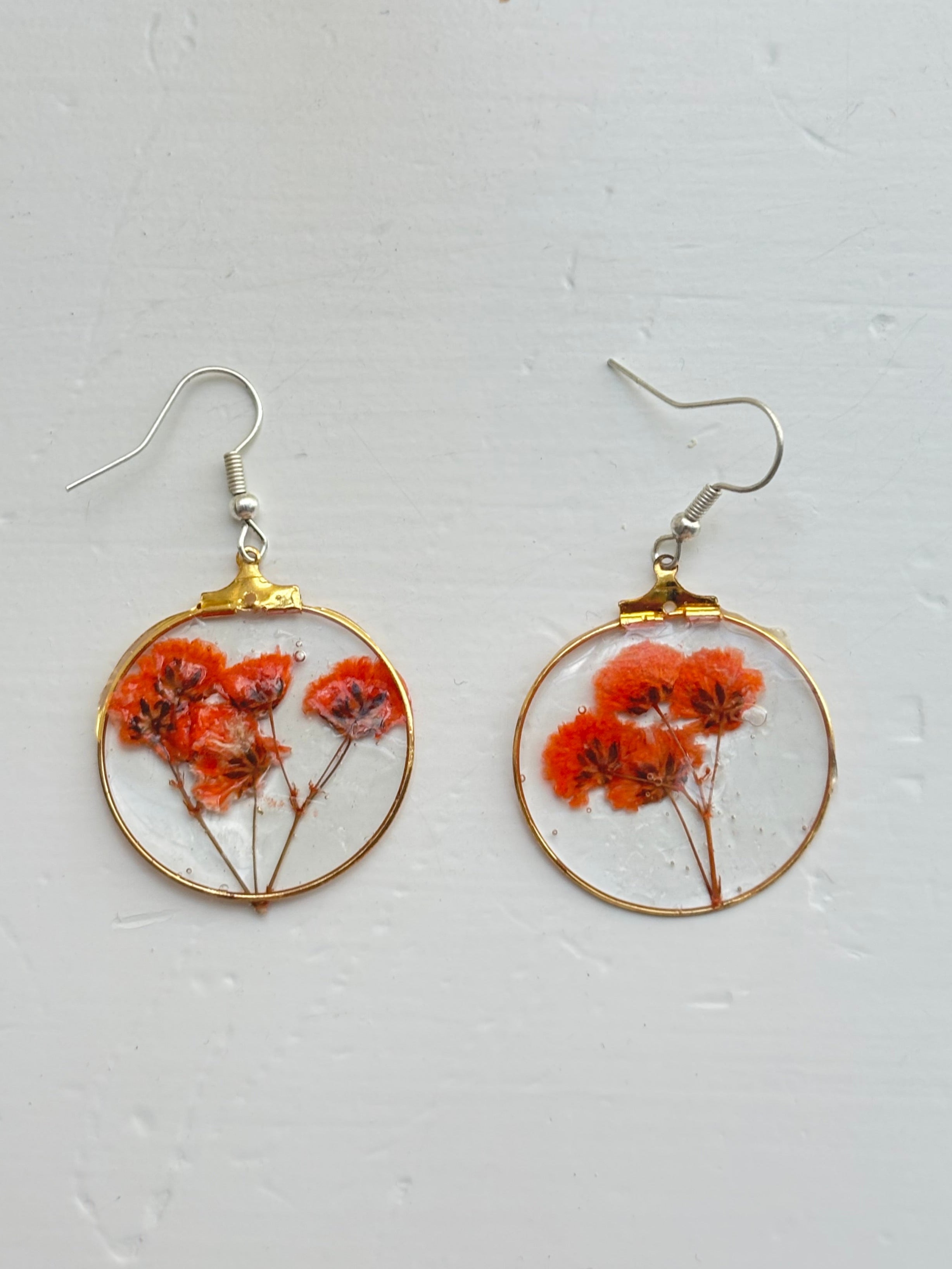 Pair of earrings with orange floral elements in gold and silver frames on a light gray background